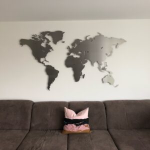 Weltkarte Edlestahl an einer weissen Wand. Unerhlab ist ein Sofa mit einem Kissen zu sehn.