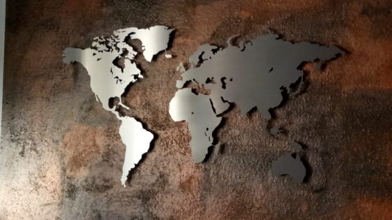 Weltkarte aus Edelstahl hängt vor einer braunen effekt Wand.