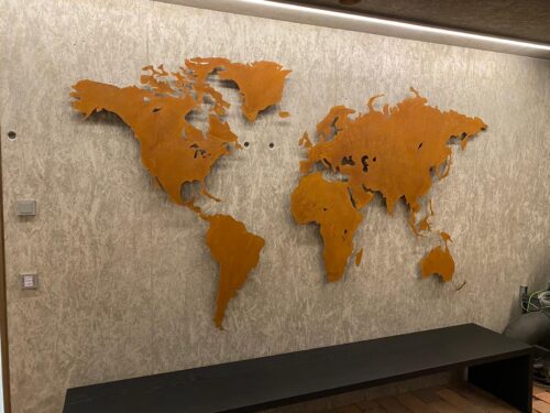Weltkarte Sonderanfertigung Rostig vor einer Betonwand. Unterhalb ist ein Sideboard zu sehen