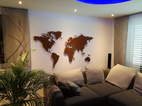 Auf dem Bild ist eine rostige Weltkarte zu sehen in einem Wohnzimmer. Sofa und ein Stück einer Pflanze ist auch zu sehen.