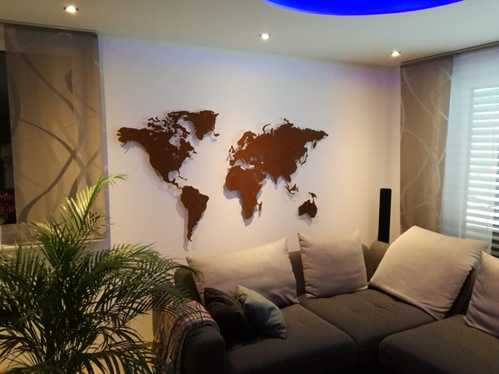 Auf dem Bild ist eine Weltkarte Rostig zu sehen vor einer weissen Wand. Es ist ein Sofa und eine Pflanze zu sehen.