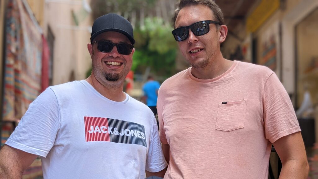 Tobias und Marcel lachen gemeinsam im Urlaub in der Sonne.