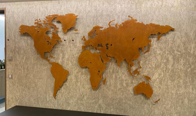 Auf dem Bild ist eine Weltkarte in einer Sonderanfertigung (extra groß) zu sehen. Sie hängt an einer betonoptik Wand.