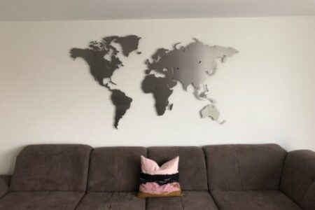 Kundenbild einer Weltkarte aus Edelstahl Größe L im Wohnzimmer an weißer Wand über grauem Sofa mit Kissen