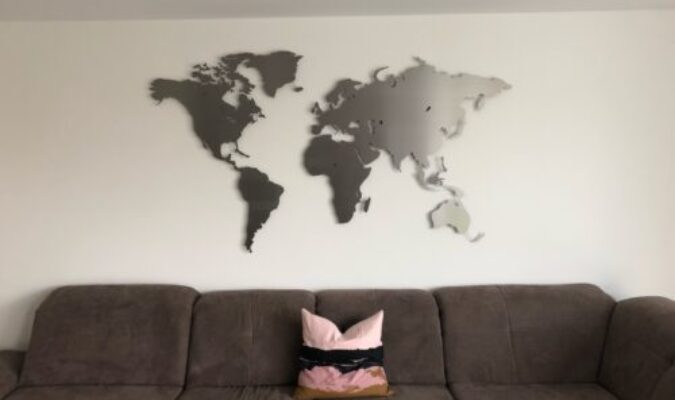 Kundenbild einer Weltkarte aus Edelstahl Größe L im Wohnzimmer an weißer Wand über grauem Sofa mit Kissen