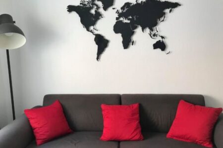 Eine Weltkarte hängt an der Wand. Unterhalb ist ein Sofa mit roten Kissen zu sehen. Es ist noch eine Lampe auf dem Bild