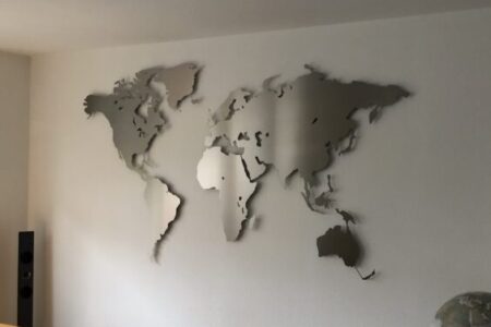 Kundenbild einer Weltkarte aus Edelstahl Größe L im Wohnzimmer an weißer Wand über gelbem Sofa