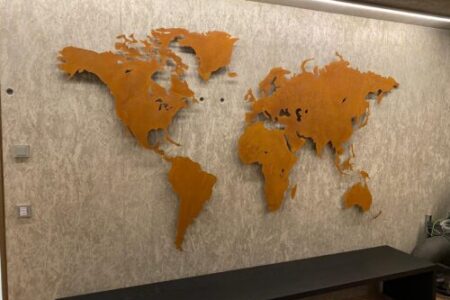 Weltkarte Sonderanfertigung Rostig vor einer Betonwand. Unterhalb ist ein Sideboard zu sehen