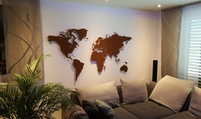 Auf dem Bild ist eine Weltkarte Rostig zu sehen vor einer weissen Wand. Es ist ein Sofa und eine Pflanze zu sehen.